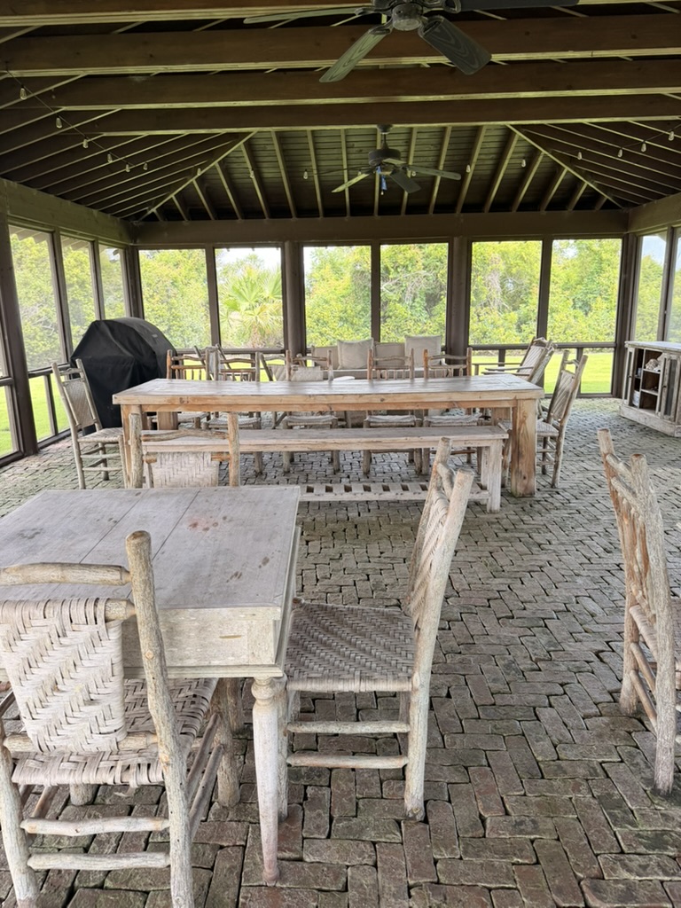 Open-air pavilion with weathered wood tables, woven chairs, and ceiling fans overlooking the marsh